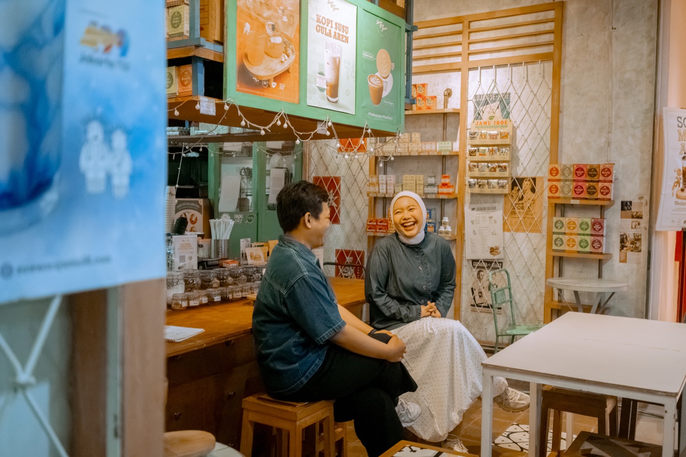 Iqbal and Deffy sitting at the herbal drink stall, laughing as they talk.