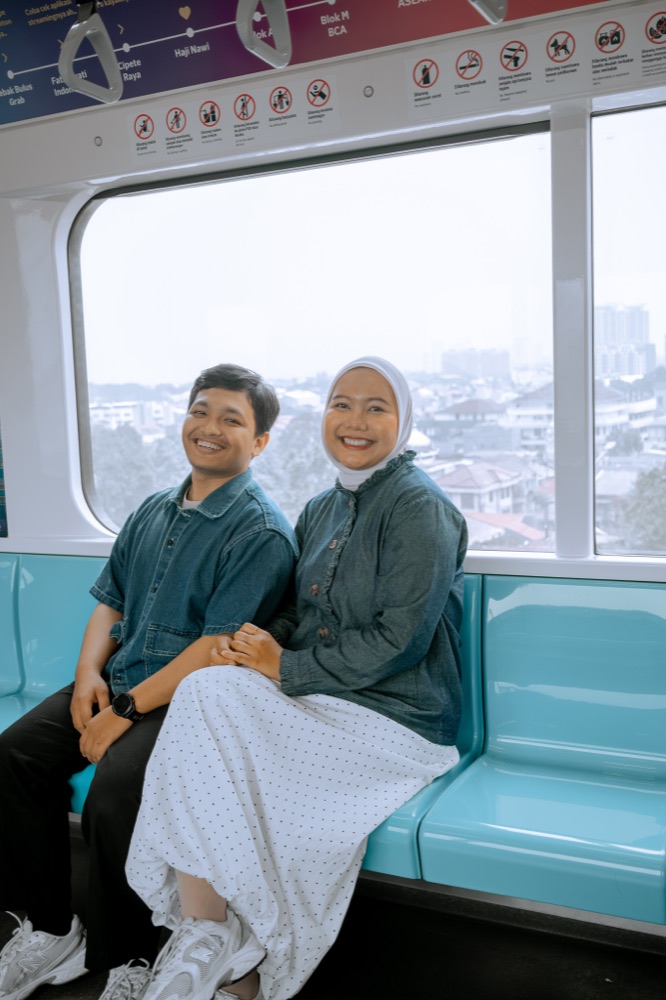 Iqbal and Deffy sitting side by side on an MRT train, smiling.